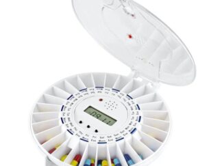 A circular pill box with a digital display at its centre and labelled compartments in a ring around the centre. The hinged lid is open and some compartments have colourful pills and tablets.