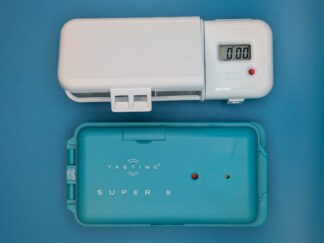Two examples of pill boxes with alarms and timers. One is white with a digital display and a hinged lid. The second is blue, with a red LED bulb and hinges open from one side.