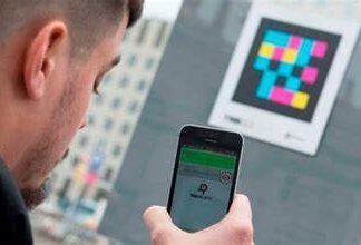Outside, someone aims their smartphone at a colourful QR code and an app on their device scans it to find more information.