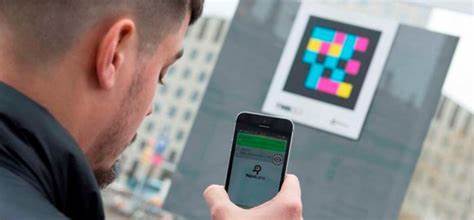 Outside, someone aims their smartphone at a colourful QR code and an app on their device scans it to find more information.