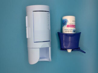 A blue tool designed to hold an eye dropper bottle laid beside a small white bottle of eye drops with a navy blue gripper at its tip.